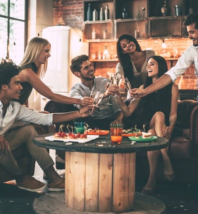 Cheers! Group of cheerful young people enjoying food and drinks while spending nice time in cofortable chairs on the kitchen together